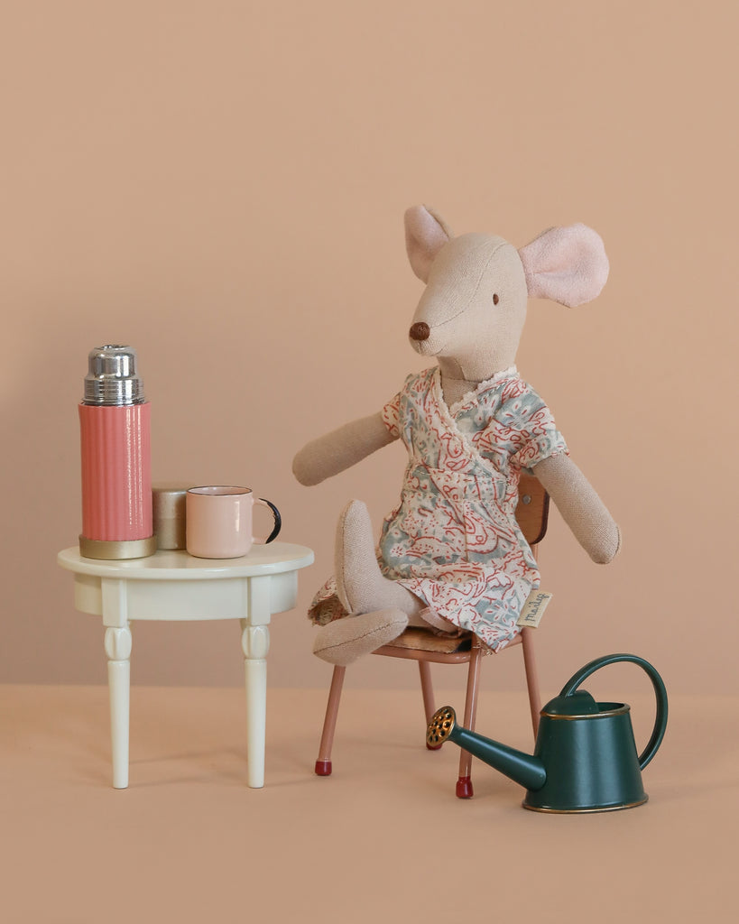 The Maileg Mom Mouse Garden Relaxation Set features a mom mouse in a floral dress on a chair beside a mini side table with a pink thermos, mug, and watering can, all against a soft beige background.