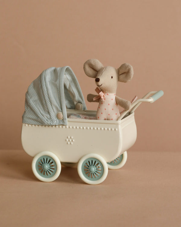 A Maileg Pram With Baby Mouse - Mint features a small stuffed mouse in a pink polka-dot outfit, seated inside a vintage-style white pram with mint and blue details, set against a beige background.