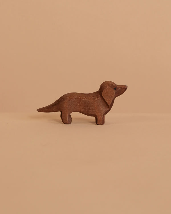 The Ostheimer Dachshund Dog, a small, handcrafted brown wooden figurine, stands on a beige surface with a matching background—ideal for imaginative play or as an addition to your Ostheimer collection.