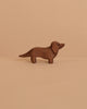 The Ostheimer Dachshund Dog, a small, handcrafted brown wooden figurine, stands on a beige surface with a matching background—ideal for imaginative play or as an addition to your Ostheimer collection.