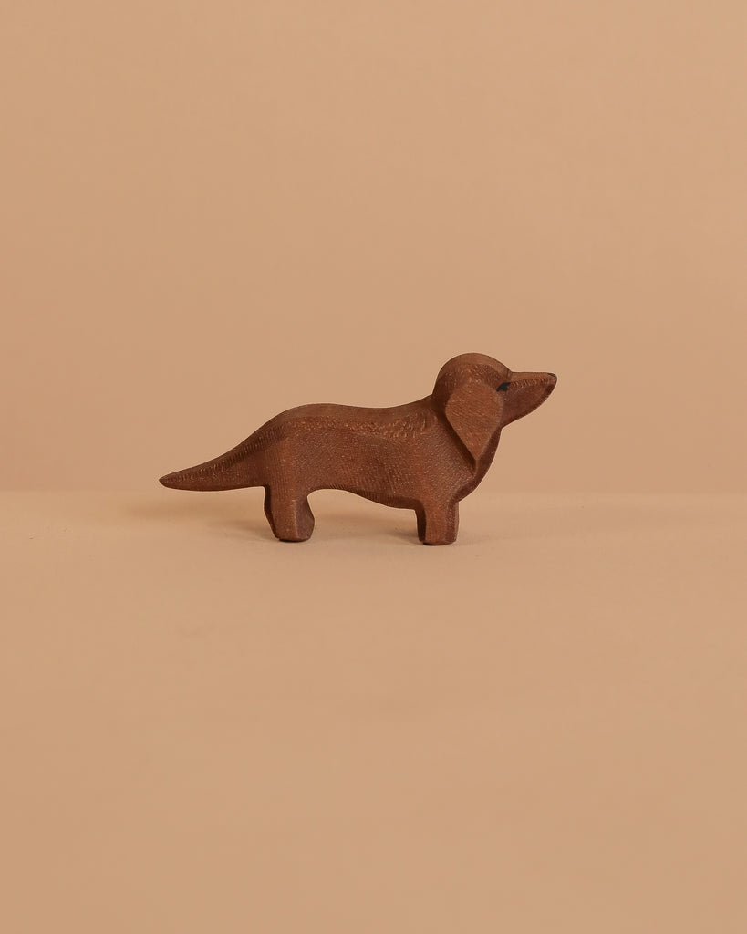 The Ostheimer Dachshund Dog, a small, handcrafted brown wooden figurine, stands on a beige surface with a matching background—ideal for imaginative play or as an addition to your Ostheimer collection.