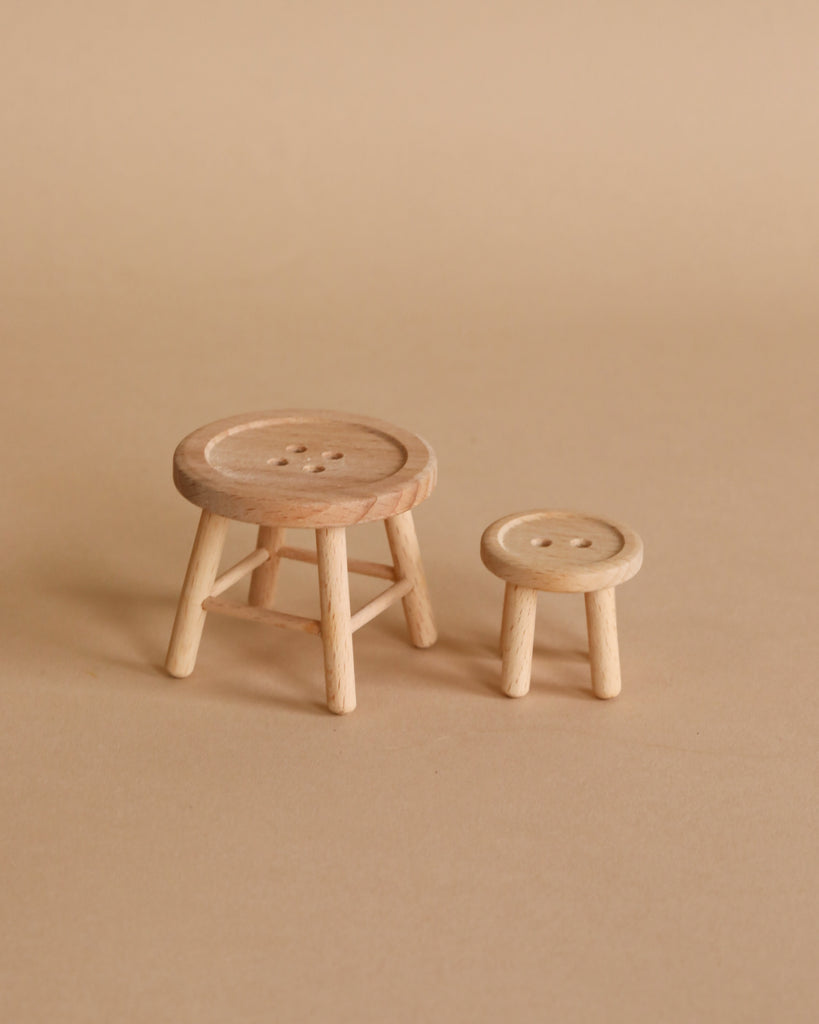 The Maileg Little Sister Bedtime Set features two small wooden stools with button-like tops—one taller with four legs and a circular seat, the other shorter—perfect as Mouse Furniture on a plain beige surface.