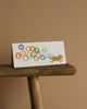 The Balloon Birthday No. 10 Card sits on a wooden table, showing a dog pulling vibrant balloons that spell "HAPPY BIRTHDAY" in gold foil against a simple beige background. Inside, the card is blank for your personal message.