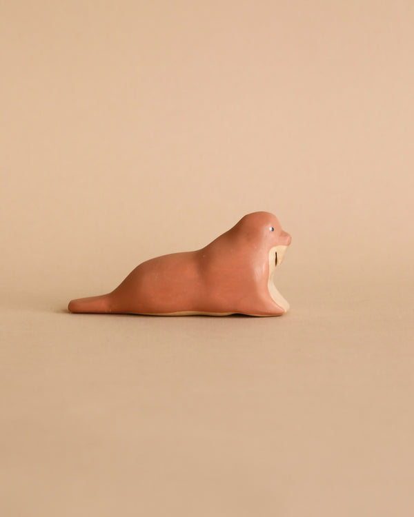 The Handmade Wooden Walrus, brown with simple features, rests on a plain matching background. Crafted like a timeless toy with child-safe paint, it captures the essence of natural beauty artfully in every detail.