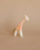 A Ostheimer Small Giraffe - Head Low figurine with orange spots and a glossy finish stands against a plain beige background.