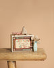 The Maileg Nursery Set With Mice features two small mice, one in blue pajamas and one with a pink blanket, posed with a vintage-style "Baby Twins Safety Matches" matchbox on a wooden stool against a beige background.