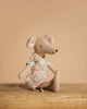 A Maileg Mom Mouse With Extra Outfit - Petite Couture rests on a wooden surface against a beige background. Wearing a light blue, patterned dress, she faces right in side view, adding charm to the scene.