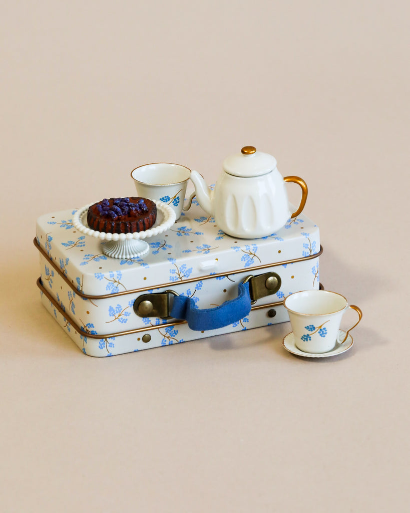 The Maileg Moms Afternoon Tea Set comes in a small suitcase with a blue floral pattern, featuring a teapot, creamer, teacups, and a plate with berries. Choking hazard: not suitable for young children.
