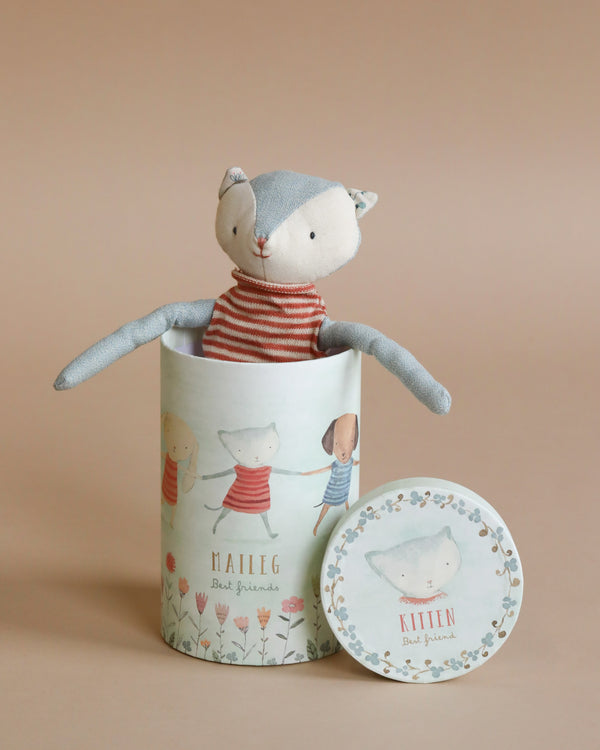 A cuddly toy, this Maileg Best Friend - Cat with a light blue head and beige body is dressed in a charming red and white striped shirt. Peeking out of a cylindrical gift box adorned with illustrations and text that reads "Maileg Best Friends" and "Kitten," it makes the perfect companion.