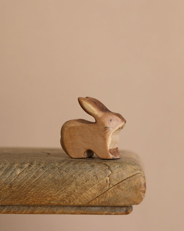 The Handmade Wooden Brown Rabbit, crafted from sustainable hardwood and finished with plant-based stains, rests on a weathered wooden surface. Its organic tones are beautifully complemented by the soft beige background.
