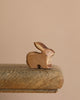 The Handmade Wooden Brown Rabbit, crafted from sustainable hardwood and finished with plant-based stains, rests on a weathered wooden surface. Its organic tones are beautifully complemented by the soft beige background.