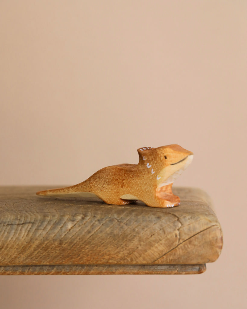 The Bearded Dragon Wooden Animal is a small, brown dinosaur figurine crafted from sustainable hardwood. It features a long tail and short legs, resting on a wooden surface against a neutral backdrop. Its glossy finish with white accents enhances its charm, resembling an intricately crafted lizard toy.