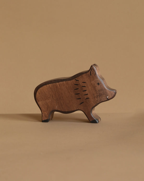 A small, carved wooden wild boar figurine named Holztiger Wild Boar stands on a flat surface. Handcrafted in Europe, its natural wood texture complements the beige background and surface, embodying simple elegance reminiscent of HOLZTIGER figures.