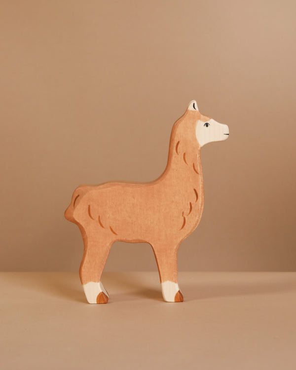 The Holztiger "Alpaca" is a handcrafted wooden figure painted light brown with white accents, set against a beige backdrop. This European-made piece embodies the charm and quality of Holztiger figures.