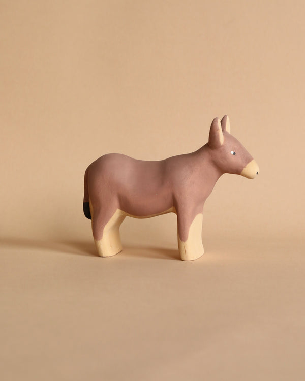 Against a tan background, the Handmade Wooden Donkey stands proudly. This charming clay figurine has a brown body with cream legs, muzzle, and inner ears. Its simple design showcases small eyes and no mouth—a testament to handcrafted linden wood artistry.