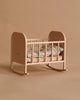 The Maileg Nursery Set features a small beige rocking cradle with slatted sides, floral bedding, and curved rockers. A Maileg Mouse peeks out playfully beside the cradle, all set against a matching beige backdrop.