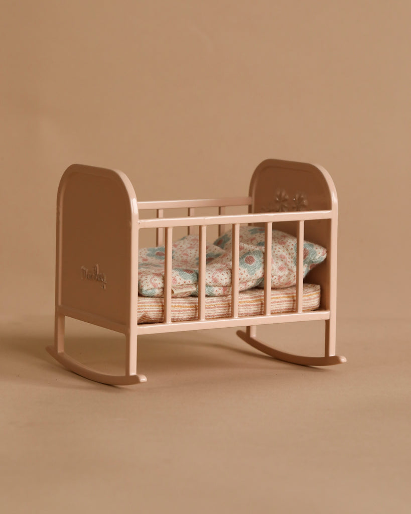 The Maileg Nursery Set features a small beige rocking cradle with slatted sides, floral bedding, and curved rockers. A Maileg Mouse peeks out playfully beside the cradle, all set against a matching beige backdrop.