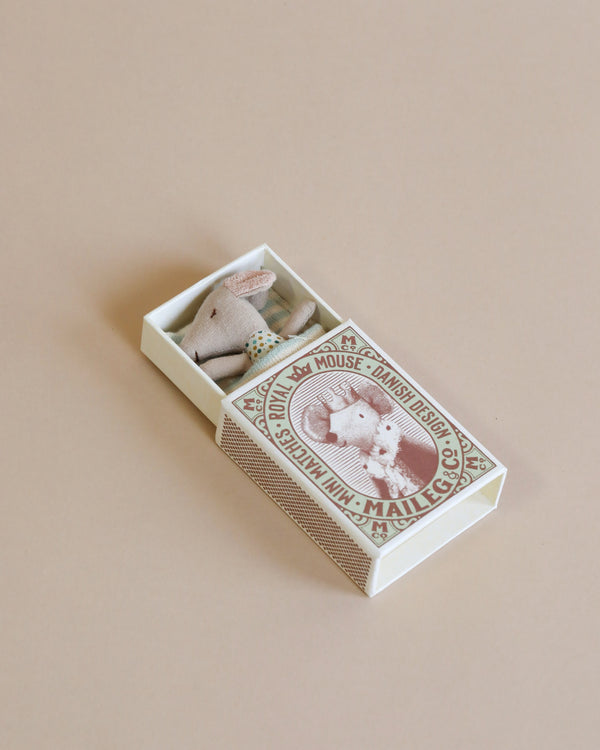 a small mouse doll inside a match box, sleeping with a blanket.