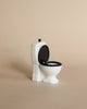 Mini white toilet with back lid. Photographed against beige background. 