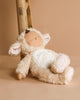 A Cozy Dinkums plush toy, the Olli Ella Cozy Dinkum Doll - Lamby Picket, leans against a wooden ladder with soft beige fur, patterned inner ears and paws, and a peaceful embroidered face. Set against a warm neutral background, it's the perfect Easter surprise plush companion.