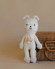 A Cuddle + Kind Llama Stuffed Animal with pink accents and a tassel belt, filled with hypoallergenic polyfill, standing in front of a wicker basket, against a beige background.
