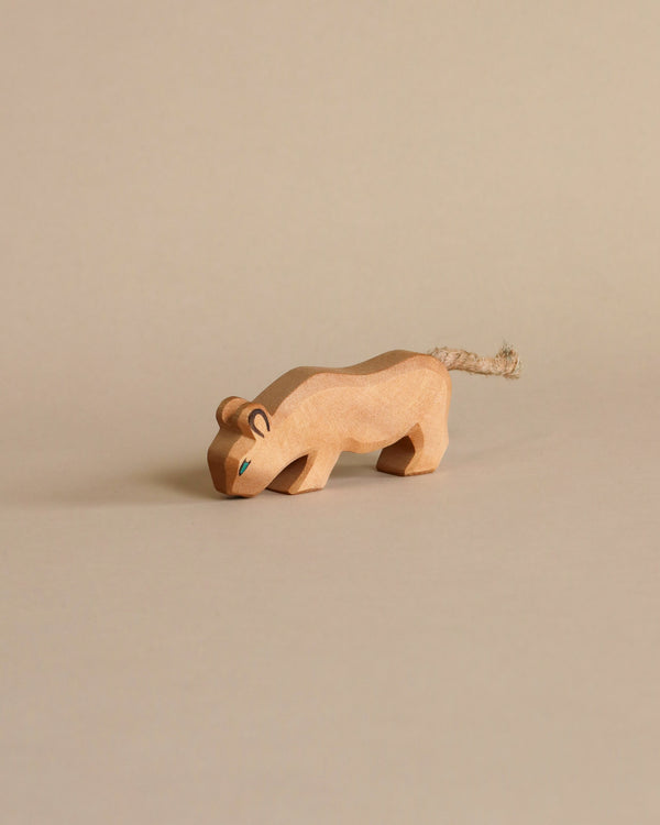 A handcrafted Ostheimer Lion toy resembling a stylized lion with a tail made from twine, positioned against a plain beige background. The lion is mid-stride, with simple features and carved details.