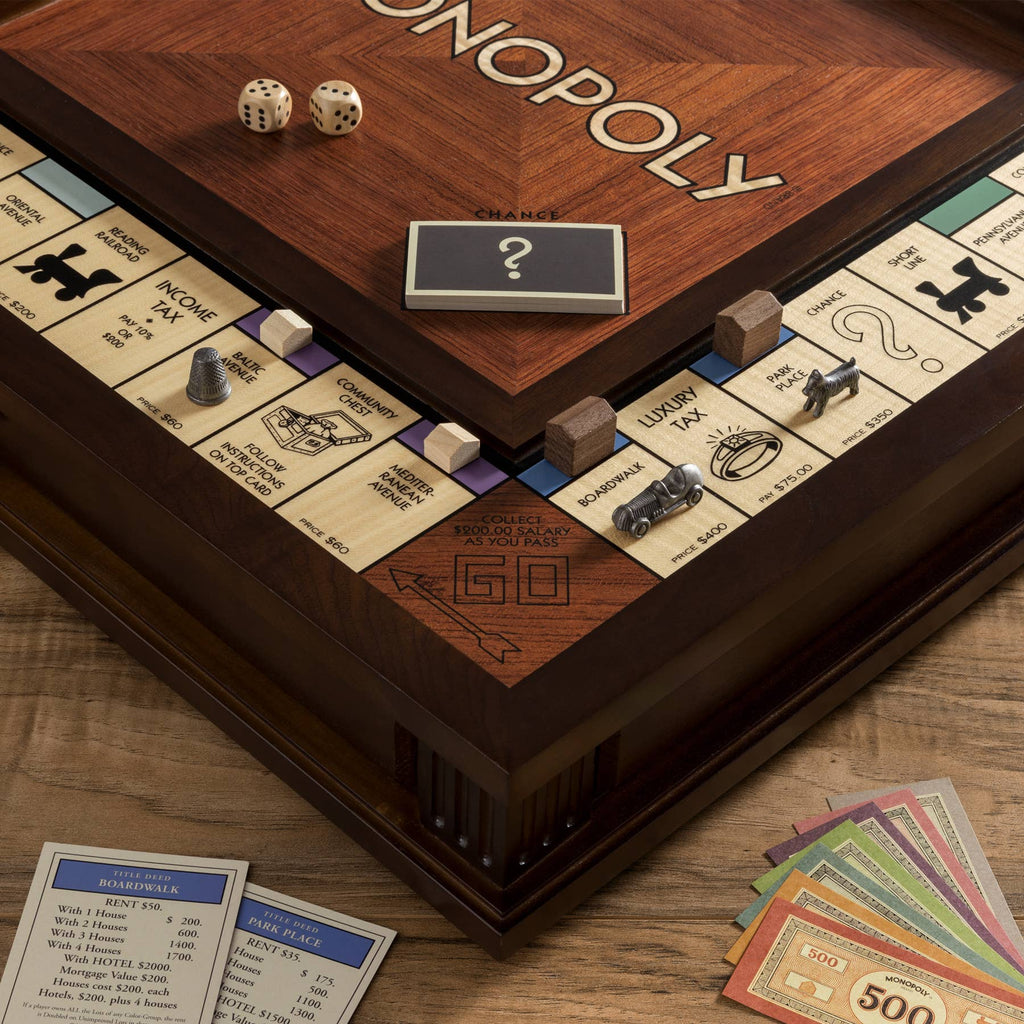 A close-up of the Monopoly Heirloom Edition wooden board features the "GO" corner, stacks of play money, cards, dice, tokens, and wooden houses and hotels. A timeless gift for every Monopoly enthusiast.
