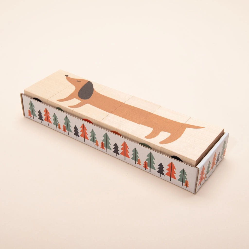 A rectangular box with a whimsical design featuring Uncle Goose Environments Neighborhood Blocks stretching along the length of the box, surrounded by a pattern of colorful basswood trees on the sides.