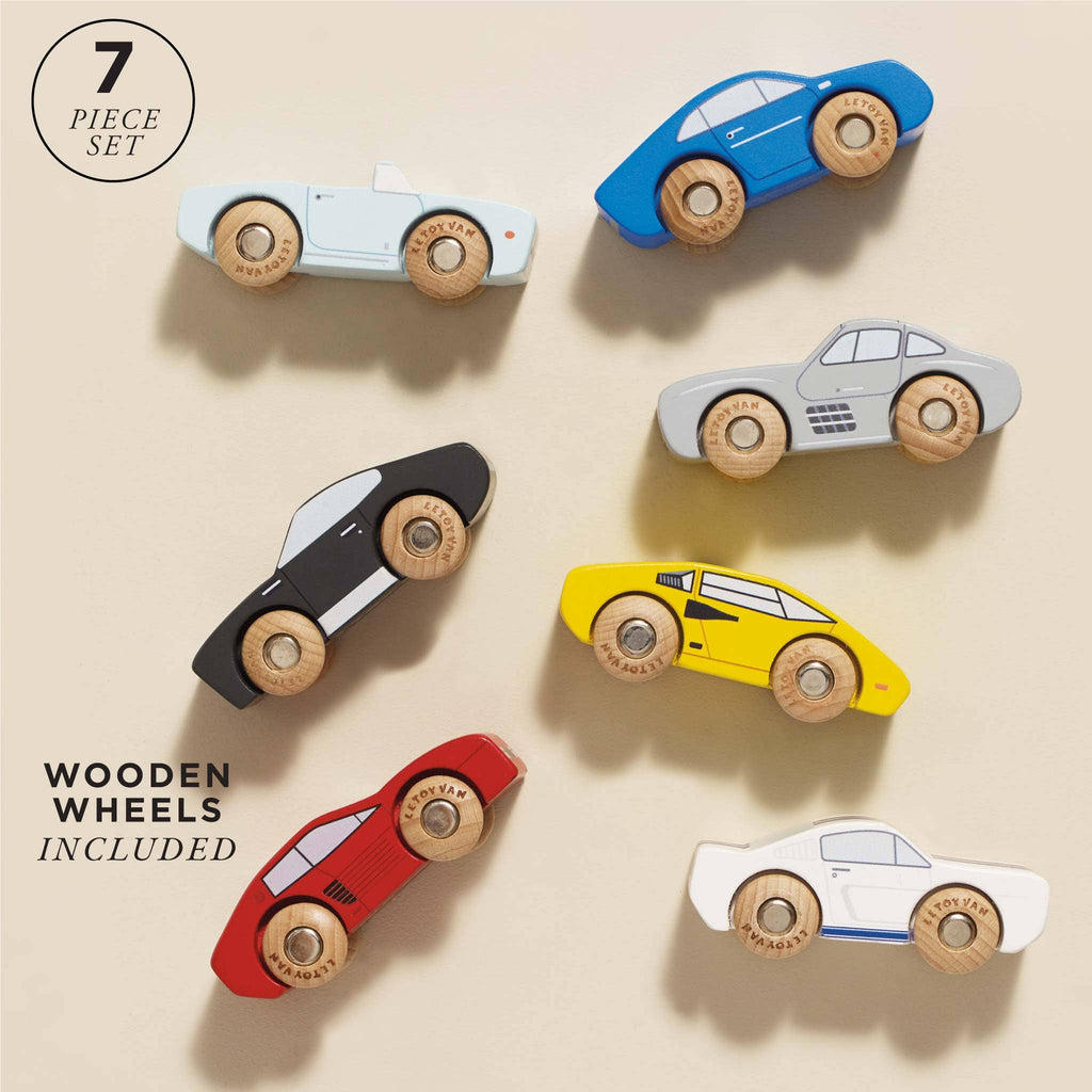 Seven Classic Wooden Sports Cars made from FSC-certified wood are displayed on a light background. The "7 piece set" text emphasizes the colorful, uniquely shaped cars with wooden wheels, designed for train track compatibility.