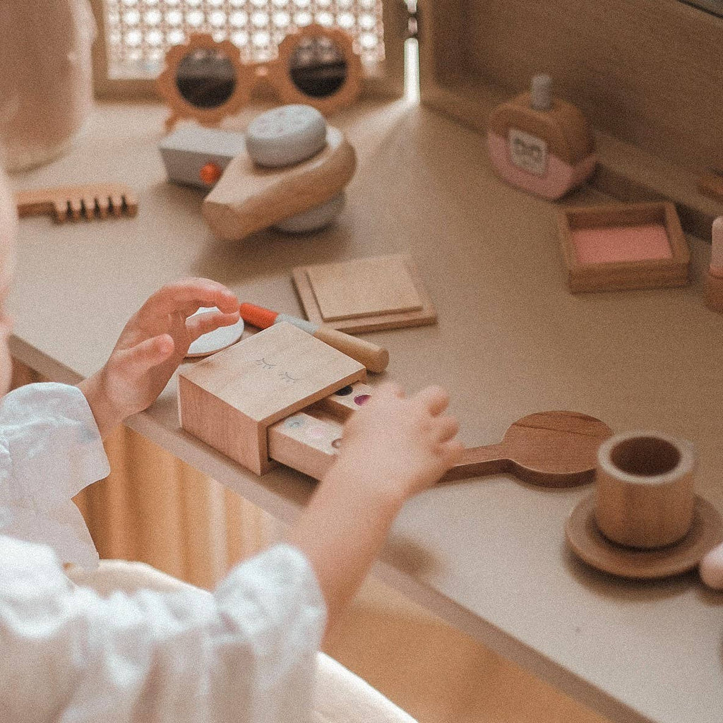 A child enjoys the Wooden Beauty Kit, a timeless toy vanity set featuring play makeup and accessories. Made with non-toxic paint in soft, neutral tones, it creates a warm and inviting atmosphere perfect for imaginative play.