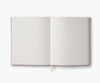 The Menagerie Embroidered Sketchbook is an open hardcover journal with blank white pages and a cream ribbon bookmark, shown from above on a plain white background.