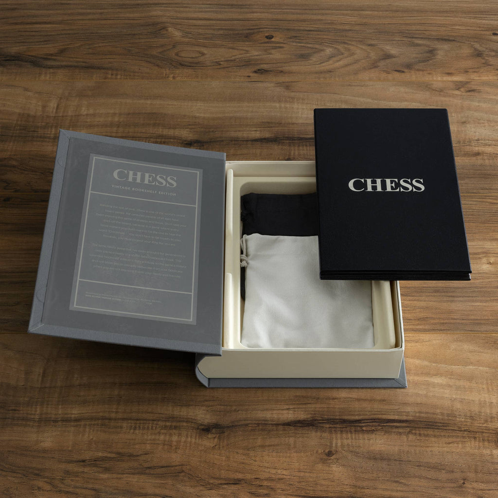 The Chess Vintage Bookshelf Edition sits open on a wooden table, displaying a cloth bag and "CHESS" booklet inside. Elegant gray and black packaging highlights the classic strategy game's timeless appeal.