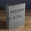 A Monopoly Vintage Bookshelf Edition box stands upright on a wooden surface, styled to look like a classic book in silver and gray with black graphics and premium components inside.