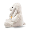 The Steiff Hoppie Bunny Stuffed Animal sits upright in profile, featuring long floppy ears, a small tail, and a yellow tag attached to one ear.