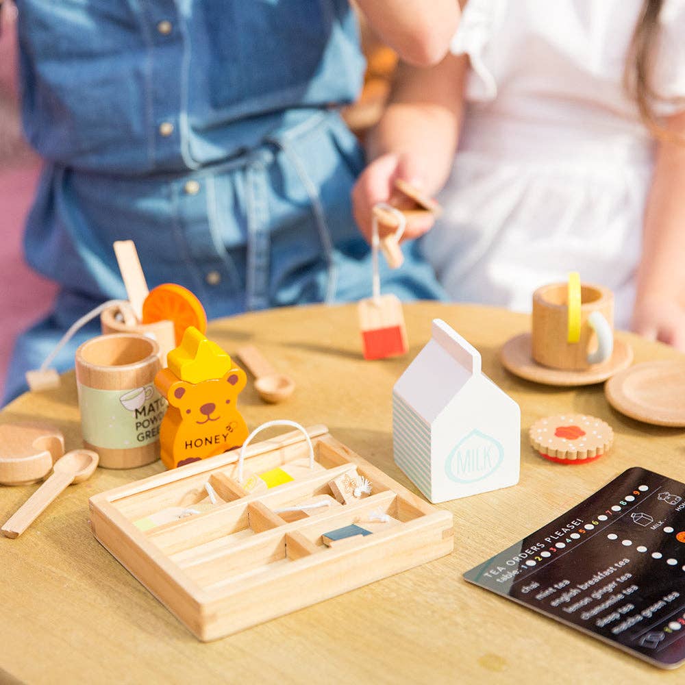 Children enjoy an imaginary tea party in their play space with the Wooden Tea Set, which includes cups, saucers, a honey bear container, milk carton, and an organic Matcha Tea box.