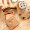 The Wooden Beauty Kit, a timeless toy set on a light wooden surface, includes a compact with a smiling face, makeup brush, comb, and beauty tools. It features natural wood finishes with minimal non-toxic paint details.