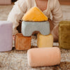 A baby plays on a carpet with Soft Toy Blocks—safe, non-toxic toddler toys in pastel colors like yellow triangle and light blue arch, inspired by Montessori blocks for fun and learning.