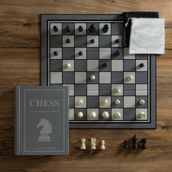 The Chess Vintage Bookshelf Edition features a collectible chess set with a gray and white board, black and white pieces, a closed book-style box labeled "CHESS," and two drawstring pouches to store this classic strategy game.