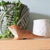 A small Bearded Dragon wooden animal, crafted from sustainable hardwood, sits on a wooden surface. Behind it, a plant in a decorative pot with leaf patterns stands alongside a white candle holder adorned with star shapes.