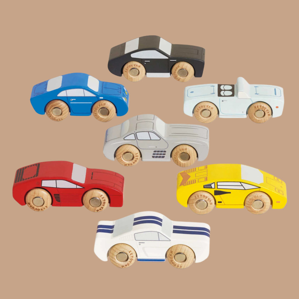 Seven vibrant toy cars from the Classic Wooden Sports Cars series, crafted from FSC-certified wood, are displayed diagonally on a beige background. The collection features wooden-wheeled designs in blue, black, striped white and blue, grey, red, white, and yellow.