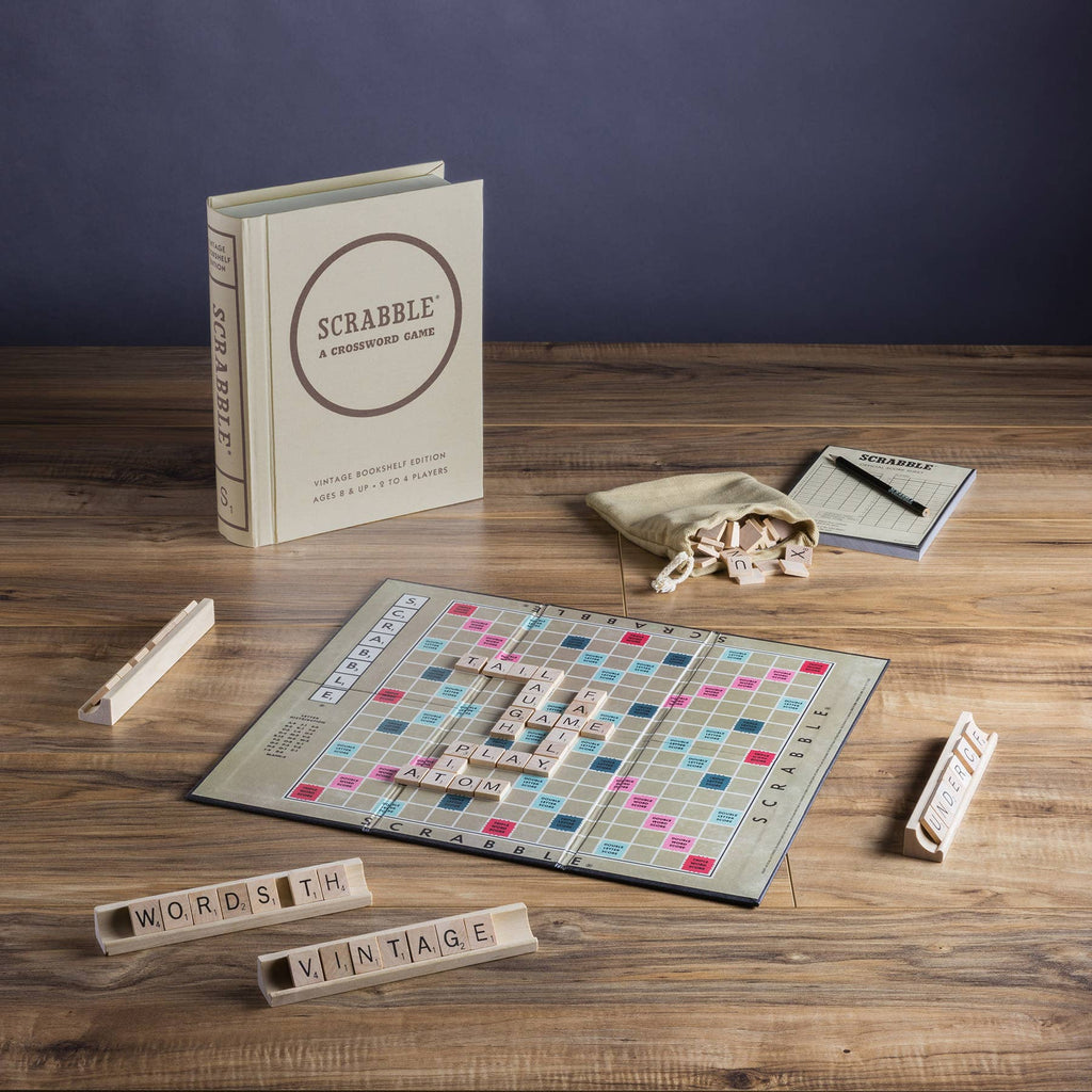 A Scrabble Vintage Bookshelf Edition is displayed on a wooden table, with its premium board, wooden racks, letter tiles, scorepad and pencil, tile bag, and box all neatly arranged.