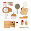 A flat lay of the Wooden Beauty Kit showcasing a hairdryer, mirror, powder compact, eyeshadow palette, brush, lipstick tubes, and perfume bottle. All items are crafted from wood with non-toxic paint in soft hues of pink and white.
