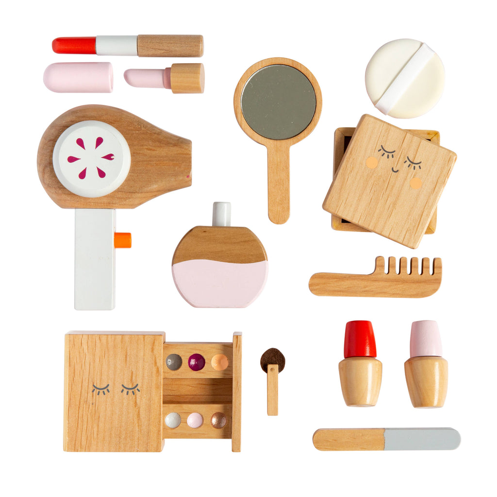A flat lay of the Wooden Beauty Kit showcasing a hairdryer, mirror, powder compact, eyeshadow palette, brush, lipstick tubes, and perfume bottle. All items are crafted from wood with non-toxic paint in soft hues of pink and white.