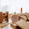 The Wooden Beauty Kit is a charming keepsake toy that includes a mock lipstick, nail polish, compact mirror, eyeshadow palette, and perfume bottle. Made from timber with natural tones, it sits elegantly on a table as soft curtains filter gentle natural light.