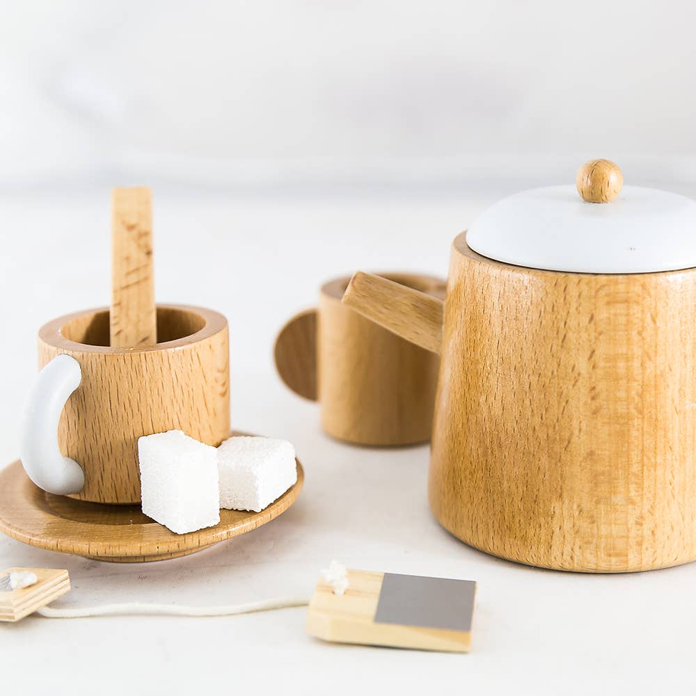 The Wooden Tea Set is a charming addition for playdates, featuring a teapot, two mugs, a sugar dish with block-shaped sugars, and a wooden teabag. It’s elegantly displayed on light surfaces similar to those in designer coffee table books.