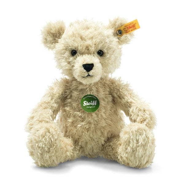 The Steiff Teddy Bear - 12" is a plush, light beige bear with black eyes, a black nose, a yellow ear tag with the stainless steel "Button in Ear," and a green "Steiff Original" tag on its chest. It sits upright against a white background.