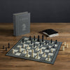 Chess Vintage Bookshelf Edition: A classic strategy game featuring white and black pieces on a board, a standing chess instruction book, and two drawstring bags—all elegantly arranged for collectors.