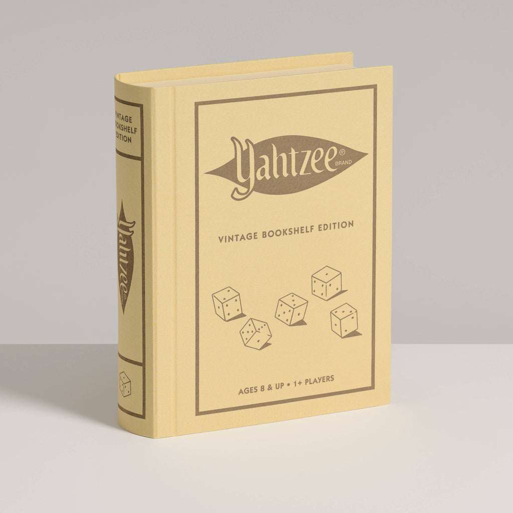 A yellow book-shaped box labeled "Yahtzee Vintage Bookshelf Edition" with illustrated dice on the cover stands upright on a white surface against a light gray background—ideal for fans of this classic vintage dice game.