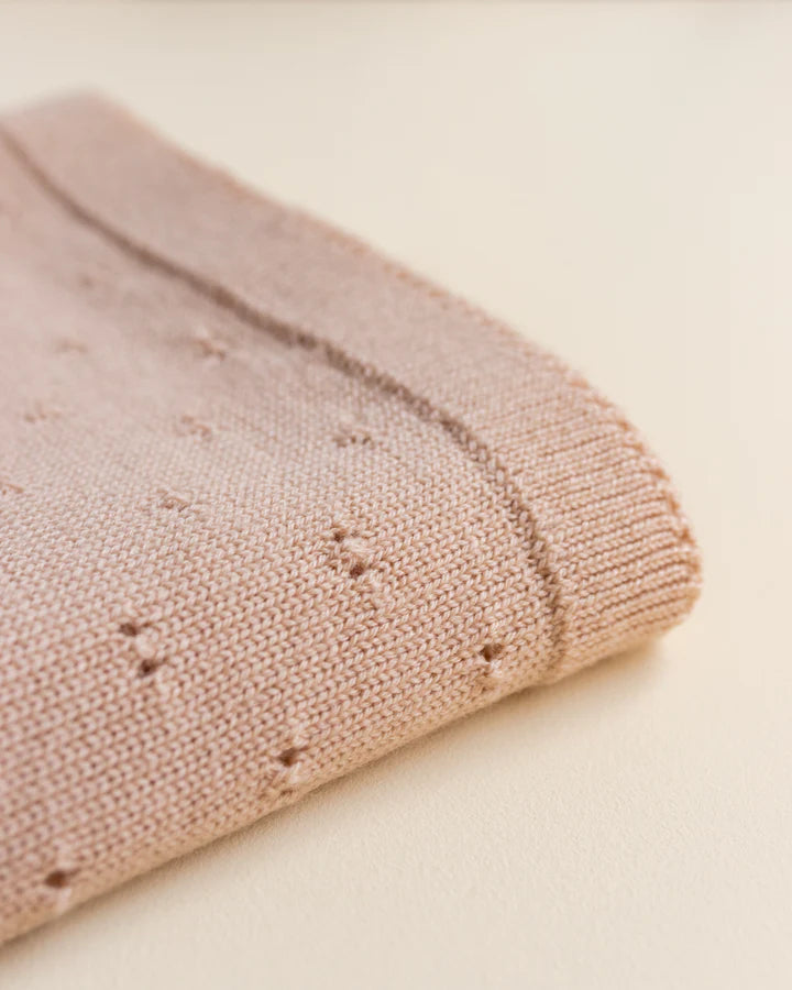 Close-up of a folded Handmade Merino Wool Bibi Blanket - Apricot with a textured knit pattern, showing delicate details on a soft beige background.