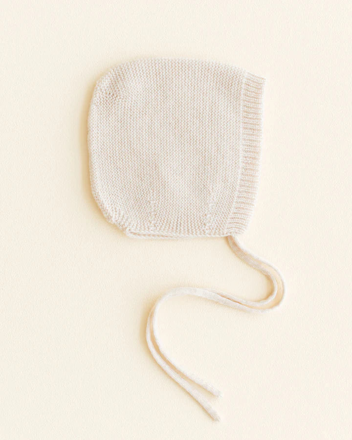 A Cream handmade Merino Wool newborn bonnet with a pair of string ties, placed on a soft beige background.